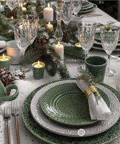 the table is set with green and white dishes, silverware, candles, and pine cones