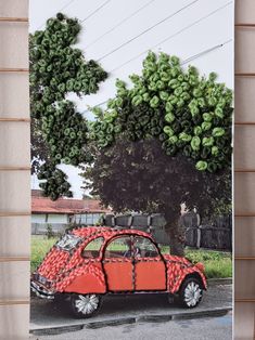 an orange car made out of plastic bottles is parked in front of a tree with green leaves