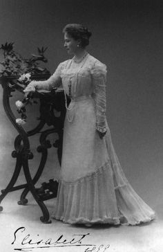 an old photo of a woman standing next to a iron fence with flowers on it