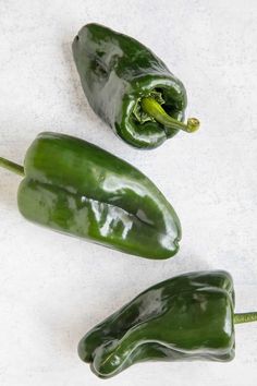 three green peppers sitting next to each other on a white counter top, with one pepper still in it's pod