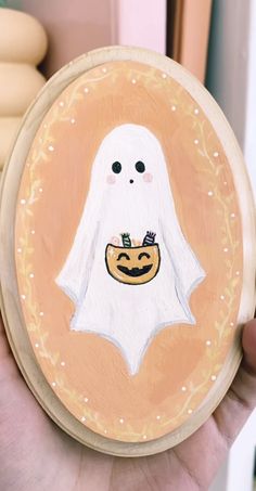 a hand holding a painted wooden plate with a ghost on it