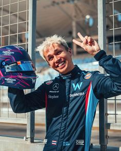 a man with blonde hair wearing a blue jacket and holding his hand up in the air