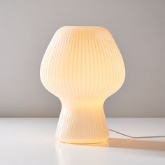 a white lamp sitting on top of a table next to a light bulb in the shape of a vase