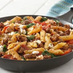 a skillet filled with pasta, meat and spinach on top of a table