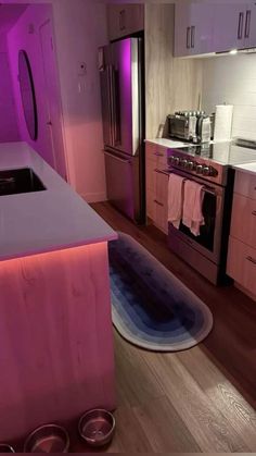 a kitchen with purple lighting and stainless steel appliances in the center, along with wooden flooring