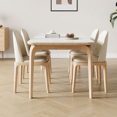 a dining table with four chairs and a plant in the corner next to it on top of a hard wood floor