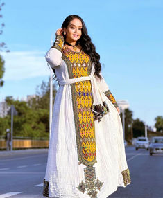 a woman in a white and yellow dress is standing on the side of the road