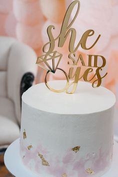 a white cake topped with a gold she said yes topper