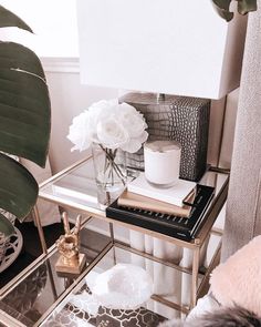 a glass table with flowers and books on it next to a plant in a vase