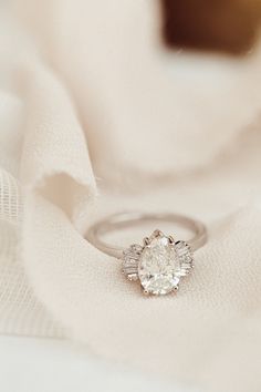 a diamond engagement ring sitting on top of a white cloth with a light colored background