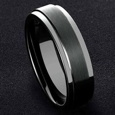 a black and white wedding band with a silver center on a black surface, the ring is