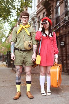 a man and woman dressed in costumes standing next to each other on the sidewalk with luggage