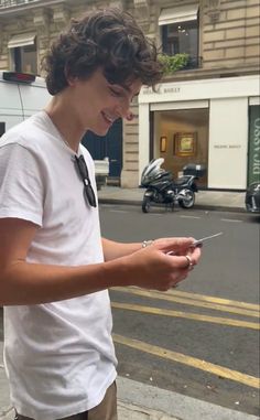 a young man standing on the side of a street holding a piece of paper in his hand