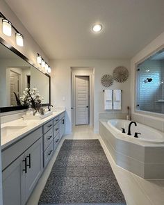 a large bathroom with two sinks and a bathtub next to a long mirror on the wall