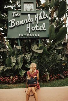 a woman sitting in front of the beverly hills hotel entrance with her purse on her lap