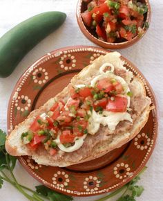 a sandwich on a plate next to a bowl of salsa and a cucumber