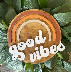 a wooden sign that says good vibes with a rainbow in the center and leaves surrounding it