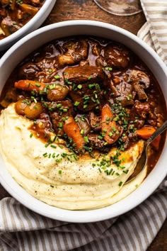 two bowls filled with mashed potatoes and beef stew on top of a wooden table