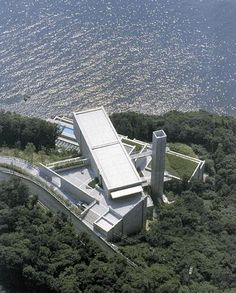 an aerial view of a building on the edge of a body of water with trees surrounding it