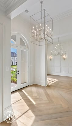 a chandelier hangs from the ceiling in an empty room with white walls and wood floors