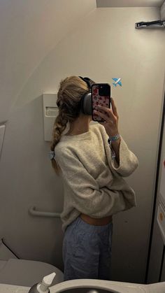 a woman taking a selfie in front of a mirror on an airplane bathroom stall