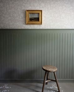 a wooden stool sitting in front of a wall with a painting on it's side