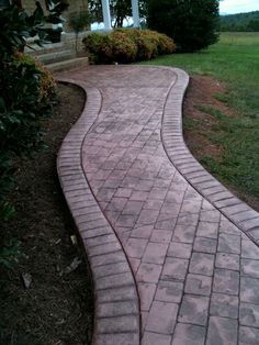 a brick walkway in front of a house with grass and bushes on the other side