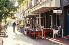 people are sitting at tables on the sidewalk in front of shops and restaurants, with one person walking down the street