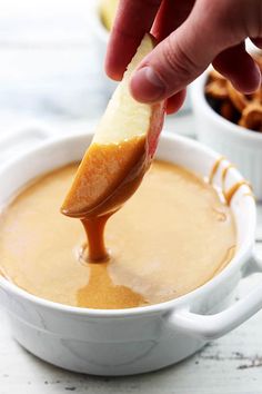 a person dipping an apple into a bowl of caramel sauce