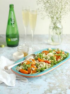 a salad with carrots and lettuce in a blue dish next to two champagne glasses