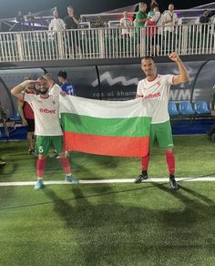 two soccer players hold up a flag on the field