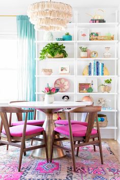 a dining room table with pink chairs and bookshelves