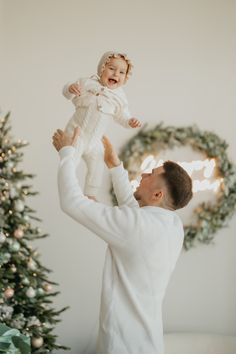 a man holding up a baby in front of a christmas tree