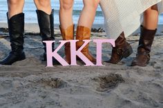 four people standing on the beach with their feet in the sand and one person wearing cowboy boots