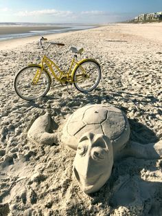 a bicycle is parked on the beach next to a sand sculpture that looks like a face