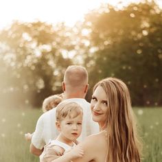 a woman sitting in the grass holding a small child with two other people behind her