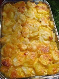 a casserole dish with potatoes and cheese in it sitting on the ground next to some grass