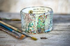 two paintbrushes sitting on top of a wooden table next to a cuff bracelet