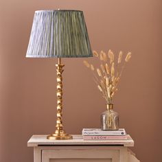 a table with a lamp, vase and books on it next to a pink wall