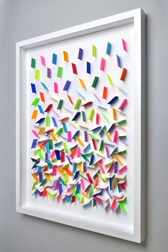 a white framed artwork with multicolored pieces of paper in the shape of squares