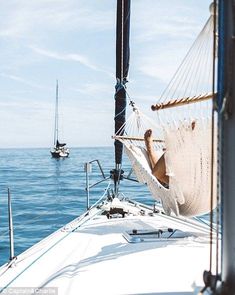 a man laying in a hammock on the back of a sailboat while another boat passes by