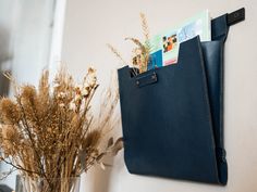 a blue purse hanging on the wall next to a vase with dried flowers in it