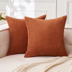 two orange pillows sitting on top of a white couch next to a vase with flowers