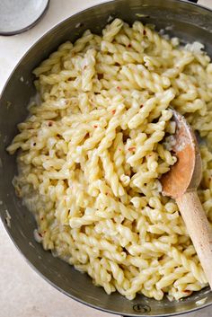 a wooden spoon in a pot full of macaroni and cheese on a table