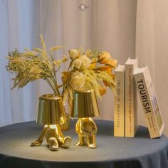 two gold elephants are sitting on a table next to books and vases with flowers in them