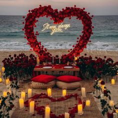 a heart - shaped sign is surrounded by candles and roses on the beach with red pillows