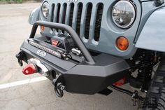 the front end of a gray jeep with its lights on and bumper mounted to it