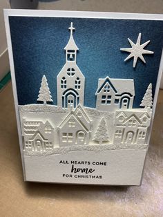 a christmas card with a church and snowflakes in the background, on a table