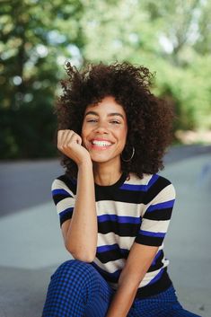 a woman sitting on the ground with her hand under her chin and smiling at the camera