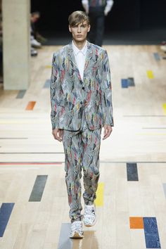 a model walks down the runway in a suit with colorful patterns on it and white sneakers